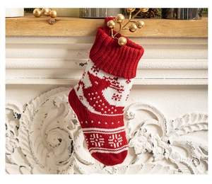 Detail of red knitted Christmas stocking with white snowflake pattern hanging on fireplace