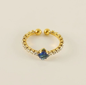 Detailed macro view of an adjustable gold-plated ring with a square blue crystal and small diamonds