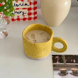 Top view of yellow ink-splatter ceramic mug with large round handle on a styled desk
