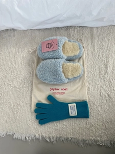Vista plana de pantuflas de felpa azules, guantes de punto y una bolsa de regalo de algodón