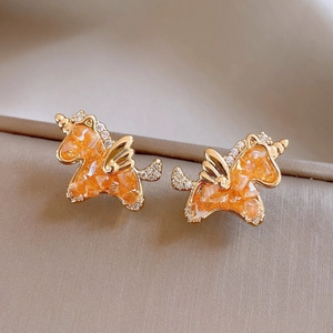 Close-up of golden unicorn stud earrings with orange gemstones on silk background