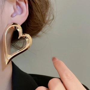Close-up of a woman wearing large gold-toned hollow heart earrings with polished metal finish