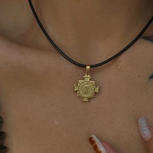 Macro view of vintage 18k gold plated cross pendant with black braided cord necklace