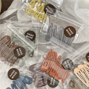 Macro detail of Morandi color teardrop hair clips in transparent zipper packaging with labels