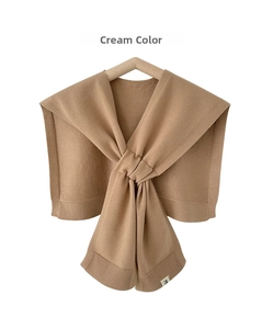 Detail view of cream-colored knitted shawl with rib-edge finish and brand logo label