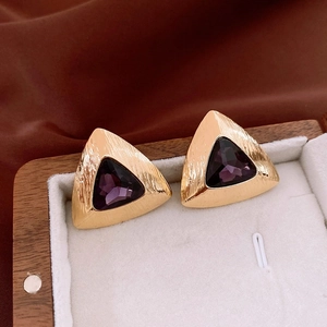 Macro shot of vintage gold triangle earrings with purple stones in a white jewelry box