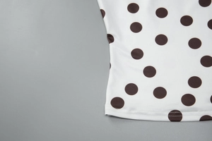 Détail du tissu blanc à pois marrons avec des coutures soignées sur l'ourlet du bas