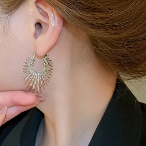 Macro shot of minimalist gold hoop earring featuring a radiating sunburst metal texture