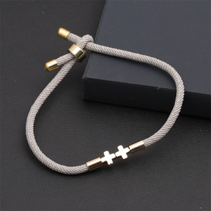 Detail of gray braided cord bracelet with two gold cross charms and adjustable metal slide buckle