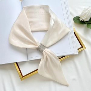 Close-up of a cream satin neck scarf with a shimmering rhinestone buckle and floral background