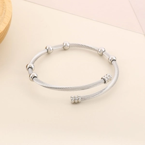 Detail of twisted cable stainless steel bangle with six polished beads on beige background