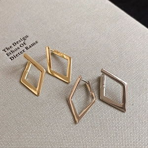 Close-up of geometric diamond-shaped huggie earrings in polished gold and silver metal finishes