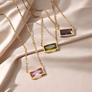 Elegant gold necklaces with rectangular purple, green, and pink gemstones on champagne silk