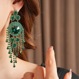 Dettaglio di orecchini vintage con nappe di strass verdi indossati su un orecchio