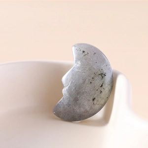 Carved labradorite moon face crystal stone leaning on a white ceramic bowl for meditation