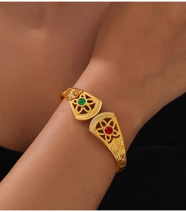 Close-up of gold hollow bangle with vintage floral pattern and red-green gemstones
