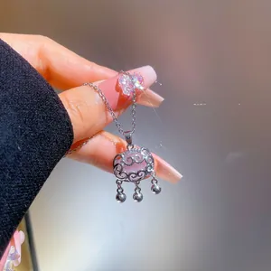Close-up of silver long life lock necklace with pink inlay and tassel bells