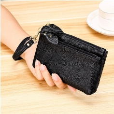 Detail of black pebbled leather coin purse with golden zippers and wrist strap