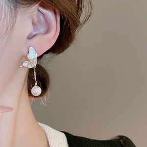 Close-up of elegant butterfly earrings with pearls and long chain on a model