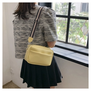 Sac bandoulière en cuir grainé jaune avec large sangle rayée porté par un mannequin