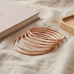 Detail showing high-polish rose gold stainless steel bangles set on soft fabric surface