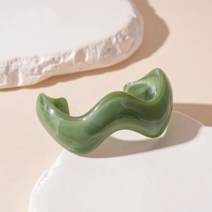 Close-up of wavy acrylic open cuff bracelet with dark green marble texture and glossy finish