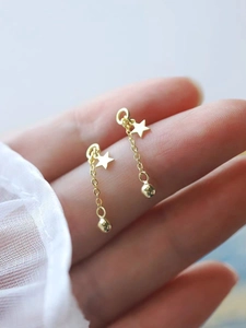 Close-up of gold star tassel earrings with chain and bead detail held by a hand