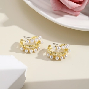 Detailed close-up of C-shaped gold metal earrings with layered white faux pearls