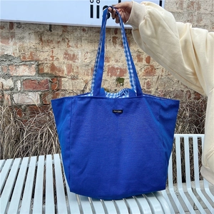 Detail view of navy canvas tote bag featuring vichy plaid lining and merciparis logo tag