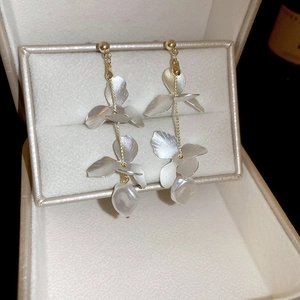 Detailed close-up of layered metal flower petals and baroque pearl on long tassel earrings