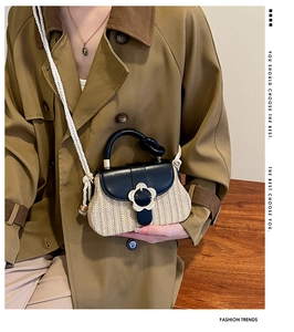 Gros plan du sac en paille tressée avec rabat en cuir noir et boucle fleurie