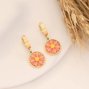 Detail of pink daisy earrings in gold finish resting on a beige tray with wheat