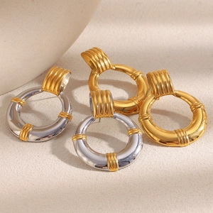 Détail des boucles d'oreilles créoles en acier plaqué or et argent sur surface texturée