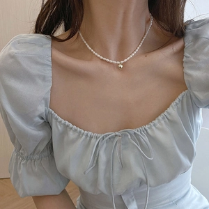 Close-up of white freshwater pearl necklace with a golden heart pendant on model