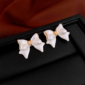 Elegant gold plated bow earrings with cream pearl glaze finish on a dark silk backdrop