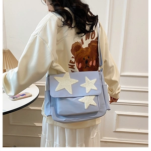 Close-up of a light blue canvas messenger bag with three plush white star patches on the flap