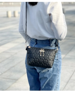 Close-up of black heart-quilted crossbody bag with a golden swan pendant and fringe detail