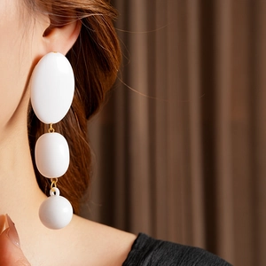 Close-up of three-tier white resin drop earrings with gold metal links on a model