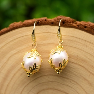 Macro shot of baroque pearl earrings with golden leaf design and zircon hooks