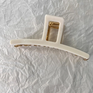 Detail of a creamy beige square hair claw clip with a golden metal spring on paper