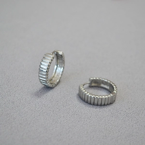 Macro di orecchini a cerchio in ottone argentato con creste verticali su tessuto grigio