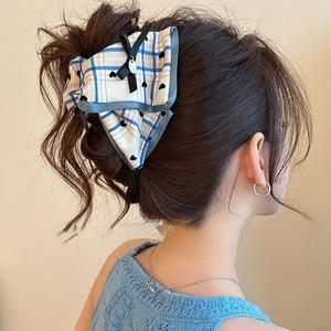 Detail of blue and white checkered bow hair claw clip worn on model's dark brown hair