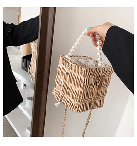 Detail of woven straw bucket bag featuring a large pearl handle and gold chain strap