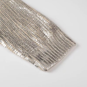Detail of silver sequin knit sweater cuff featuring ribbed texture and metallic shine
