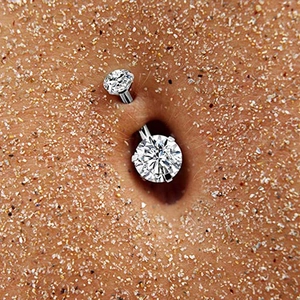 Surgical steel belly button ring with double round clear zircon on beach sand background