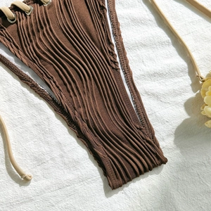 Detail of dark brown ribbed bikini fabric with metal eyelets and beige side ties