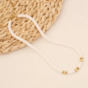 Bohemian multilayer necklace with white clay beads and gold steel spacers on a straw mat