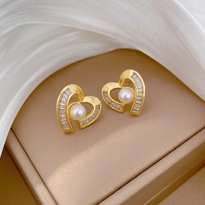 Detail of golden heart earrings with white pearls and square crystals on champagne silk
