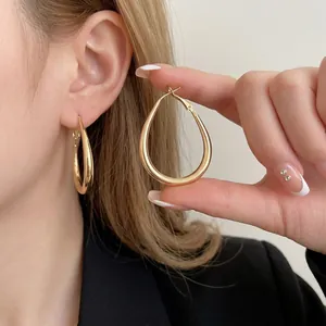 Minimalist gold teardrop hoop earrings with high polish finish worn by a model