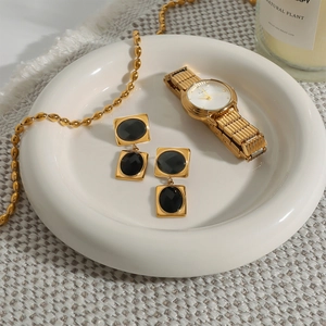 Close-up of luxury gold-plated steel earrings with black square stones on a ceramic plate